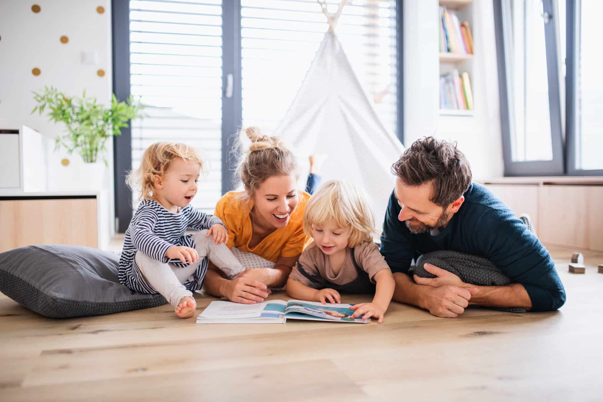 Young family with two small children reading a book together on a laminate floor